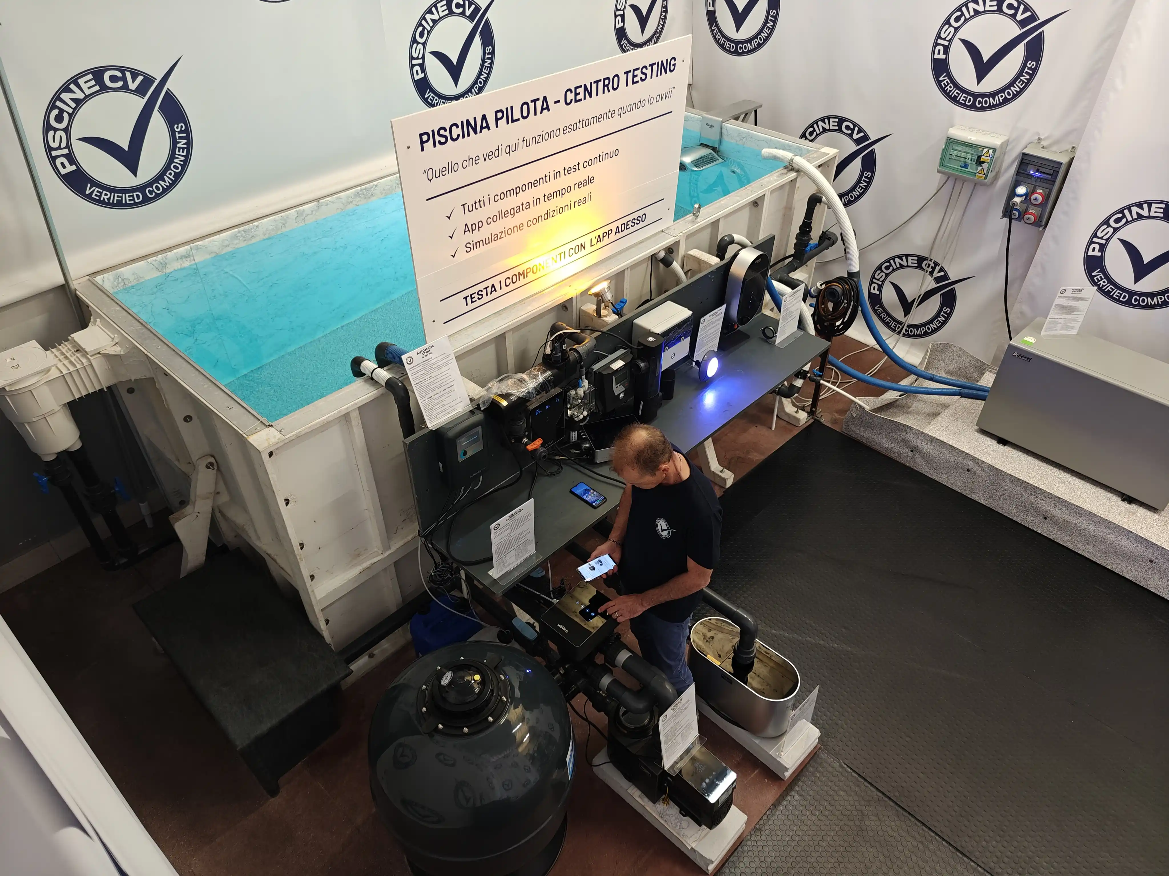 Tecnico Piscine CV nel Centro Testing con smartphone in mano, componente acceso e acqua visibile